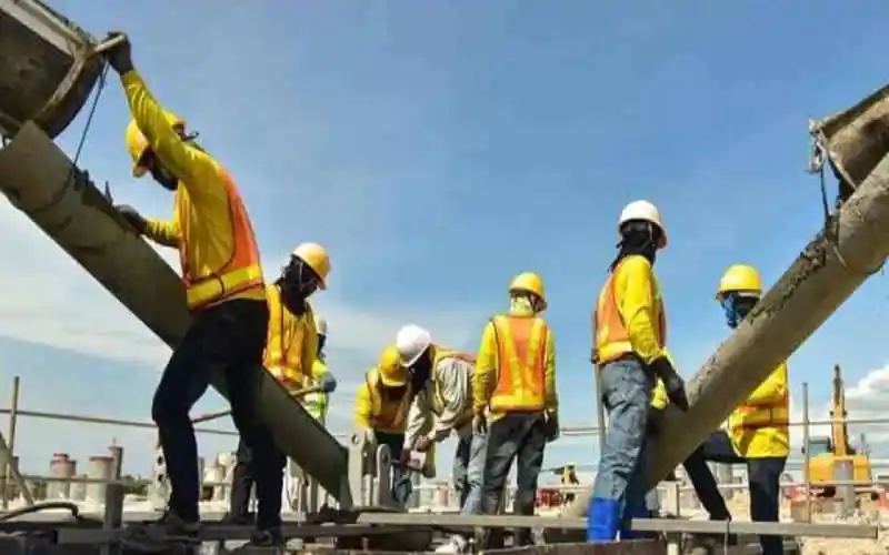 Construction workers in yellow safety vests and helmets working on a building site. Channel i News - চ্যানেল আই নিউজ