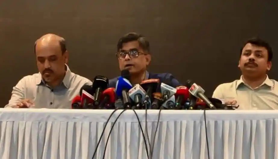 প্রেস কনফারেন্সে তিনজন কর্মকর্তা, microphones ও টেবিলের সামনে বসে. Channel i News - চ্যানেল আই নিউজ