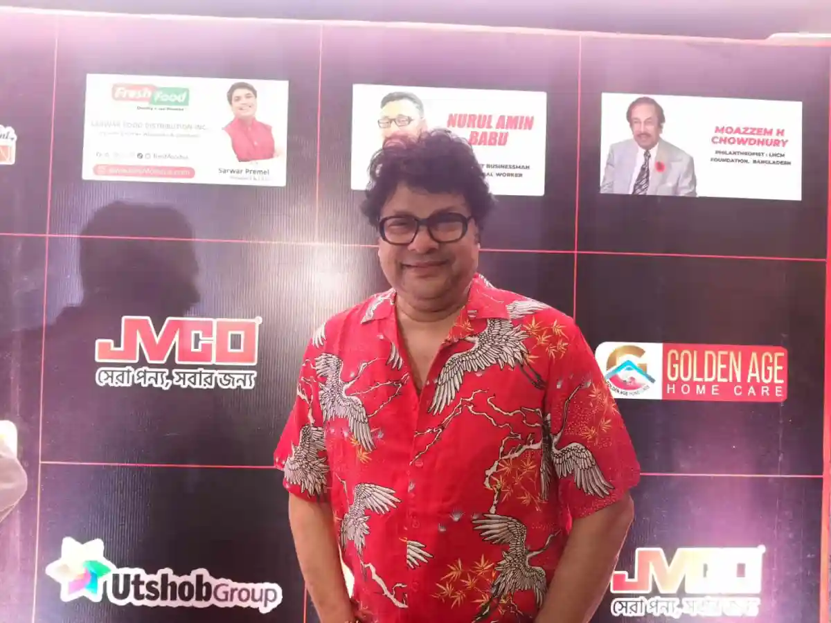 প্রেস কনফারেন্সে একজন ব্যক্তি হাসিমুখে দাঁড়িয়ে আছেন. Channel i News - চ্যানেল আই নিউজ