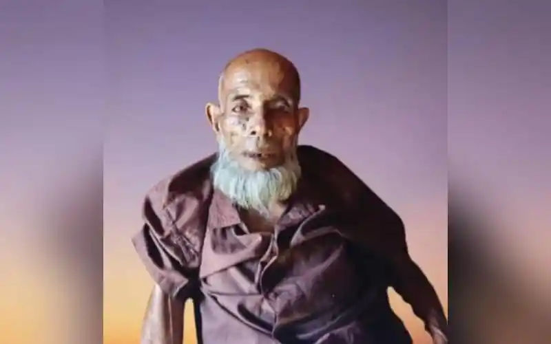 Elderly man with a white beard and traditional attire smiling at camera. Channel i News - চ্যানেল আই নিউজ