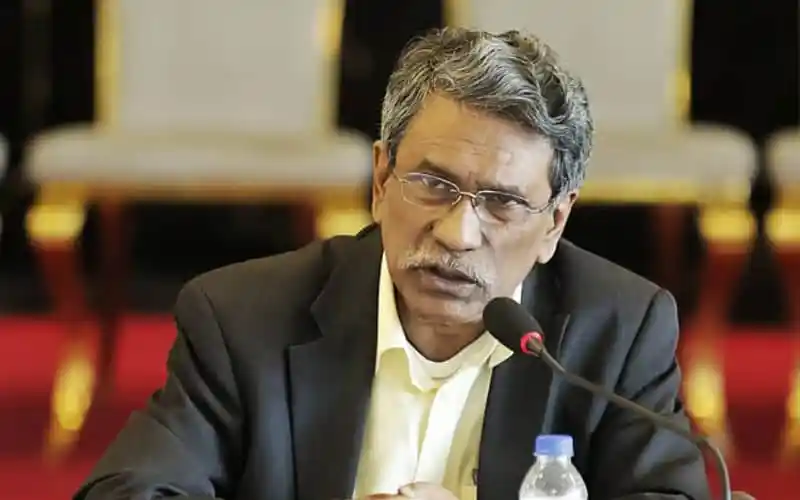 অধ্যাপক আলী রিয়াজ বক্তৃতা দিচ্ছেন, পেছনে সাদা চেয়ার দেখা যাচ্ছে. Channel i News - চ্যানেল আই নিউজ