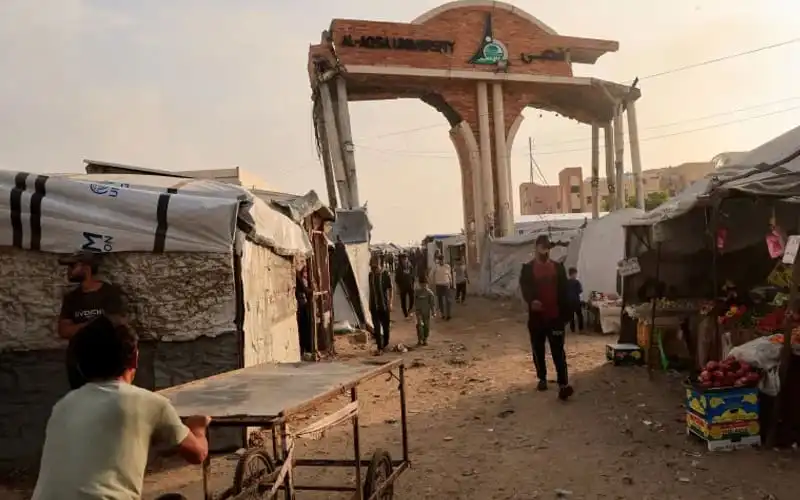 People walking through a makeshift market with an archway in the background. Channel i News - চ্যানেল আই নিউজ