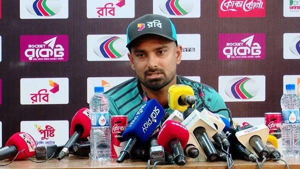 লিটন দাস সংবাদ সম্মেলনে বক্তব্য দিচ্ছেন, পেছনে বিভিন্ন সংবাদ সংস্থার লোগো. Channel i News - চ্যানেল আই নিউজ