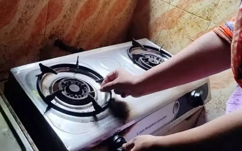 Gas stove with a person turning on the burner in a kitchen. Channel i News - চ্যানেল আই নিউজ