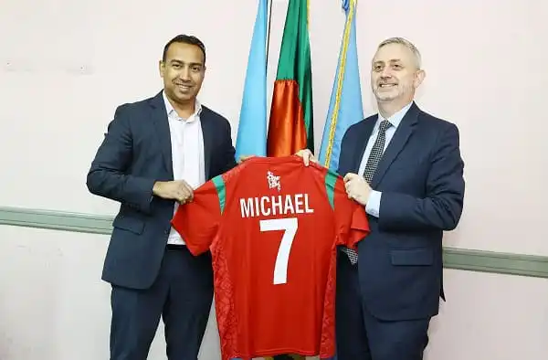 Two men holding a red football jersey with 'Michael 7' printed on it. Channel i News - চ্যানেল আই নিউজ