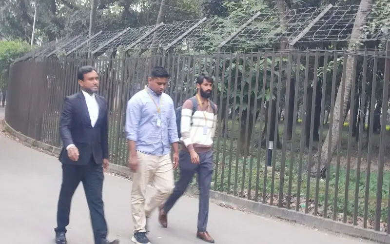 তিন ব্যক্তি জেলেপাড়ার রাস্তায় হাঁটছেন, পেছনে জাল ও তারের বেড়া. Channel i News - চ্যানেল আই নিউজ