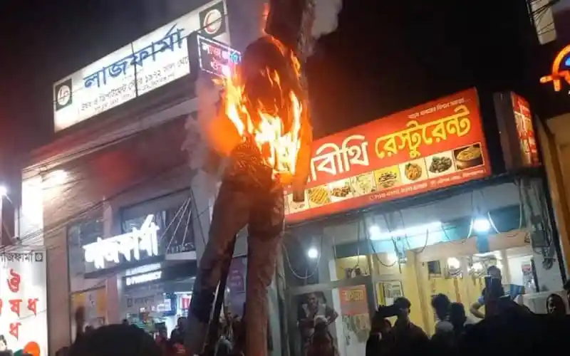 অগ্নিসংযোগের ঘটনায় একজন যুবক দগ্ধ হয়ে দাঁড়িয়ে আছেন, আশপাশে জনতা ও দোকানপাট।. Channel i News - চ্যানেল আই নিউজ