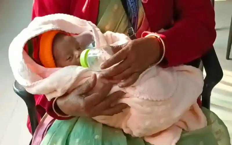 নবজাতক শিশুটি একটি দুধের বোতল খাচ্ছে, হাতে একজন নারী ধরে রেখেছেন।. Channel i News - চ্যানেল আই নিউজ