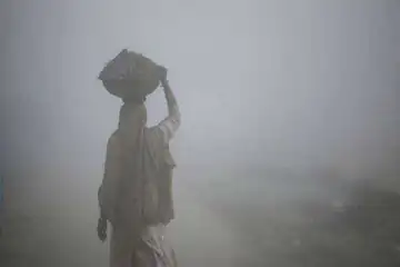 ধূসর আকাশে একজন নারী ঠাণ্ডা বাতাসে হাঁটছেন, কুয়াশাচ্ছন্ন পরিবেশ. Channel i News - চ্যানেল আই নিউজ