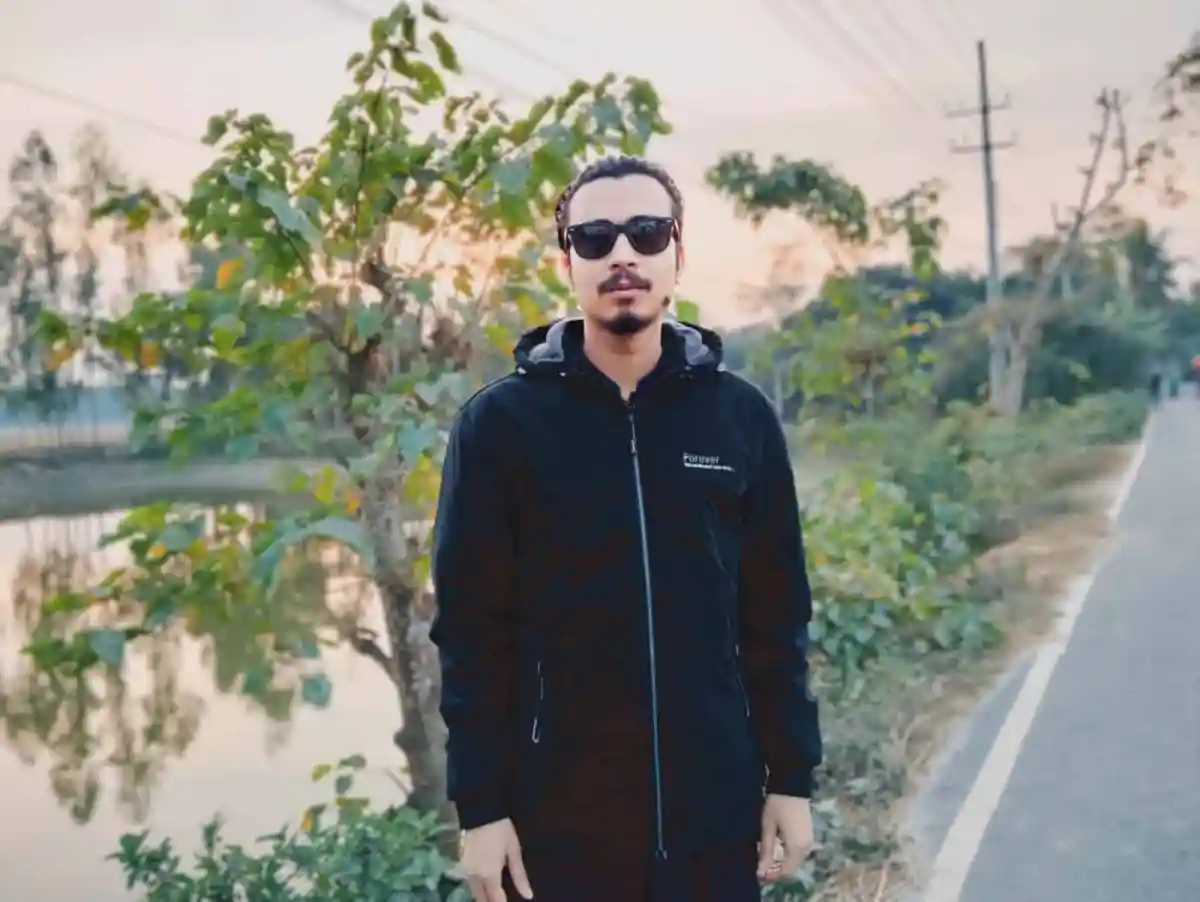 Man in black jacket and sunglasses standing outdoors during sunset. Channel i News - চ্যানেল আই নিউজ