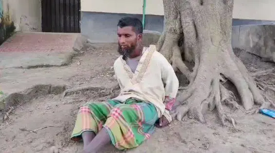 একজন ব্যক্তি গাছের নিচে বসে আছেন, আটক করা হয়েছে. Channel i News - চ্যানেল আই নিউজ