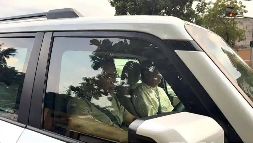 Two men sitting inside a white car, seen through the window. Channel i News - চ্যানেল আই নিউজ