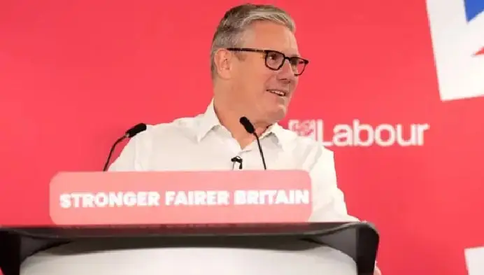 British politician speaking at a podium with Labour Party banner in background. Channel i News - চ্যানেল আই নিউজ