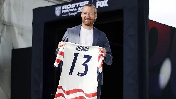 Ream holding his US national team jersey with number 13 at a sports event. Channel i News - চ্যানেল আই নিউজ