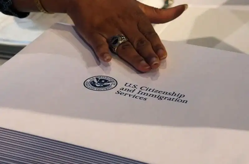 একজন ব্যক্তির হাত U.S. Citizenship and Immigration Services এর ফাইলের উপর রাখছেন।. Channel i News - চ্যানেল আই নিউজ