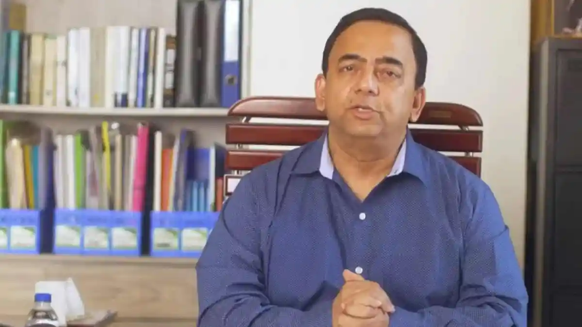 বেনজীর আহমেদ বসে আছেন, পেছনে বইয়ের আলমারি দেখা যাচ্ছে. Channel i News - চ্যানেল আই নিউজ