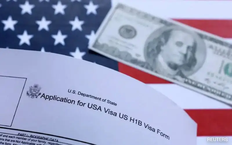 U.S. H-1B visa application form with U.S. dollar bills on an American flag background. Channel i News - চ্যানেল আই নিউজ