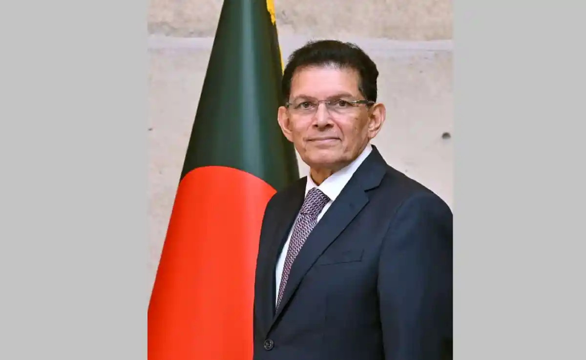 Bangladeshi official in formal suit standing beside Bangladesh flag. Channel i News - চ্যানেল আই নিউজ