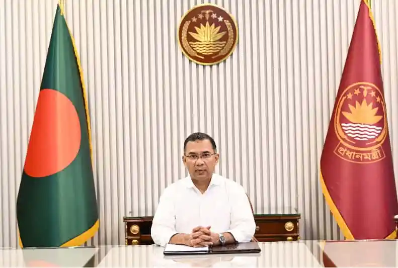 প্রধানমন্ত্রীর অফিসে বসে এক ব্যক্তি, বাংলাদেশের পতাকা ও জাতীয় পতাকা পেছনে।. Channel i News - চ্যানেল আই নিউজ