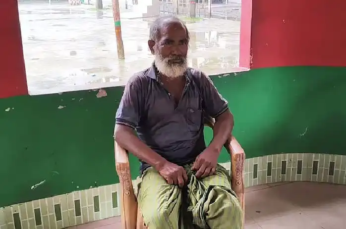 বৃদ্ধ ব্যক্তি সীমান্তের শূন্যরেখায় বসে আছেন, পেছনে বৃষ্টির দৃশ্য।. Channel i News - চ্যানেল আই নিউজ