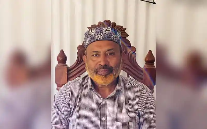 বাংলাদেশের একজন নেতা, মাথায় পাগড়ি পরা, বসে আছেন।. Channel i News - চ্যানেল আই নিউজ