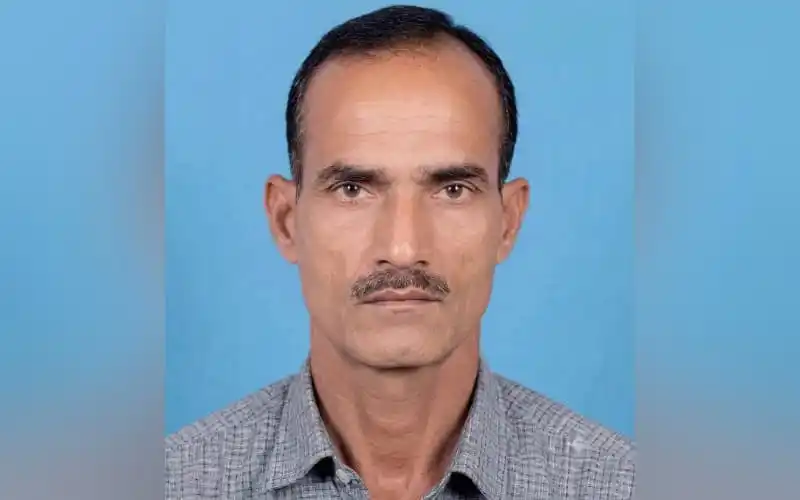 A middle-aged Bengali man with a serious expression against a blue background. Channel i News - চ্যানেল আই নিউজ