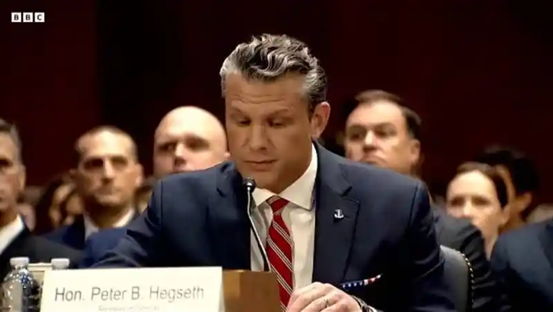 Hon. Peter B. Hegseth testifying at a formal hearing with audience in background. Channel i News - চ্যানেল আই নিউজ