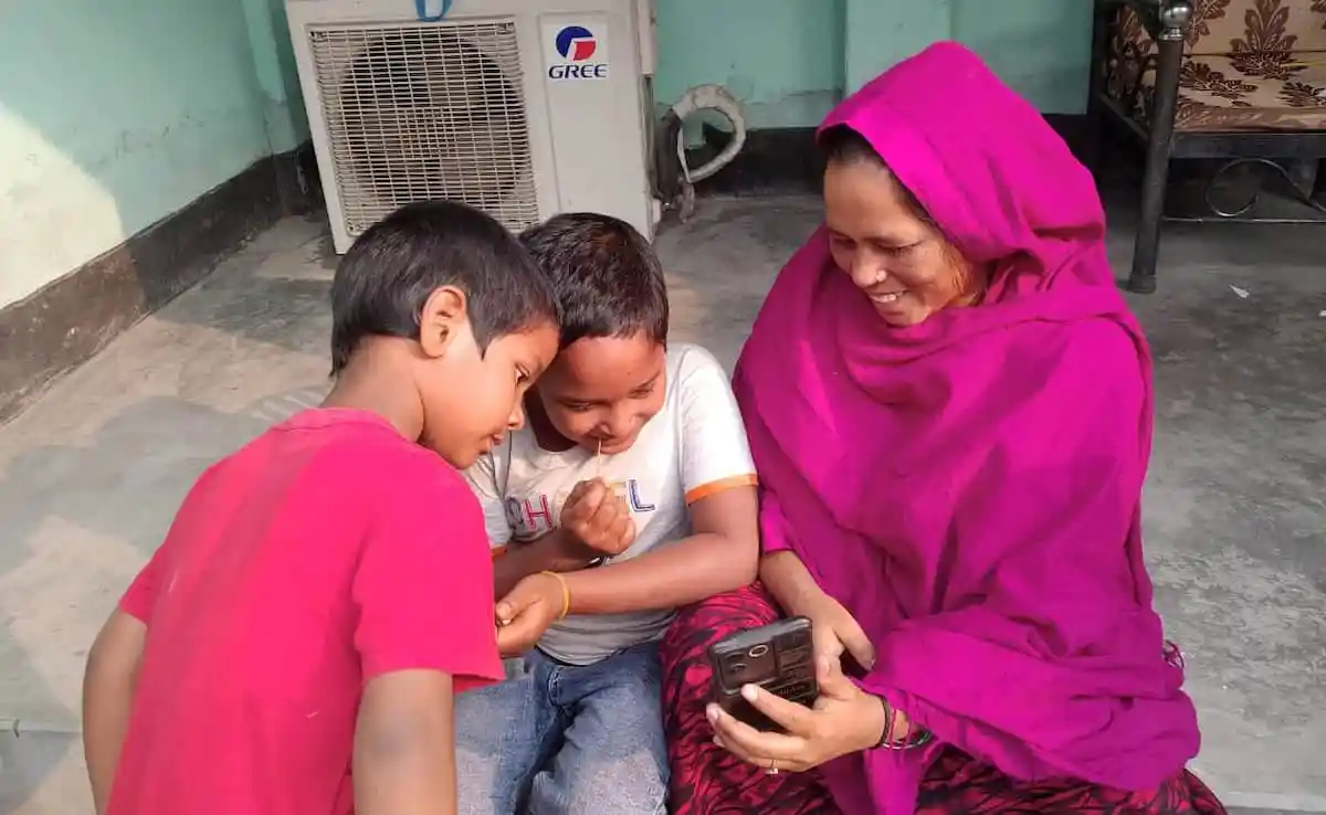 বৃদ্ধা নারী ও দুই শিশু মোবাইল ফোন দেখছে. Channel i News - চ্যানেল আই নিউজ