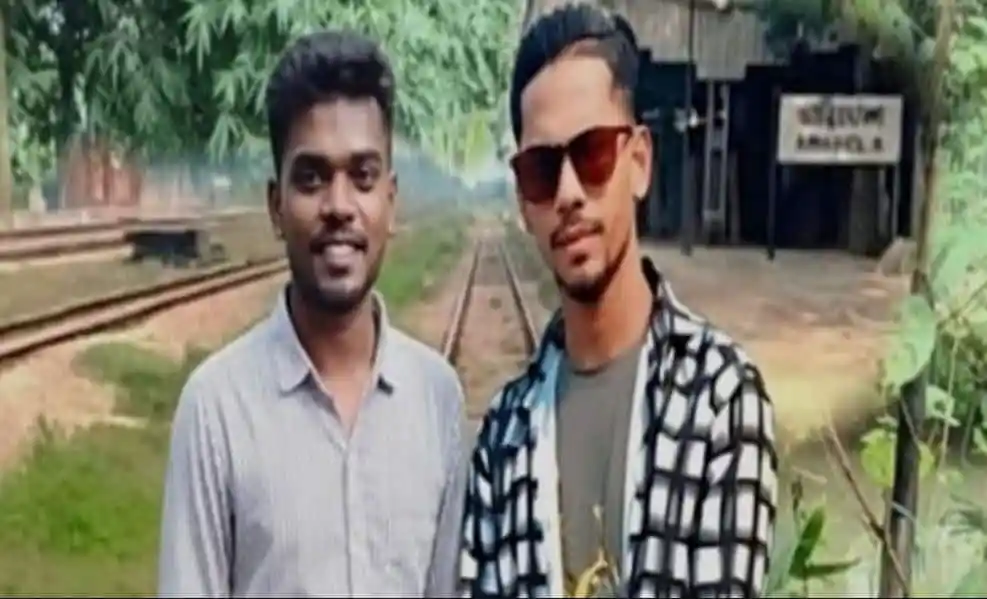 দুই যুবক রেললাইনের পাশে দাঁড়িয়ে, পেছনে ট্র্যাক ও গাছপালা. Channel i News - চ্যানেল আই নিউজ