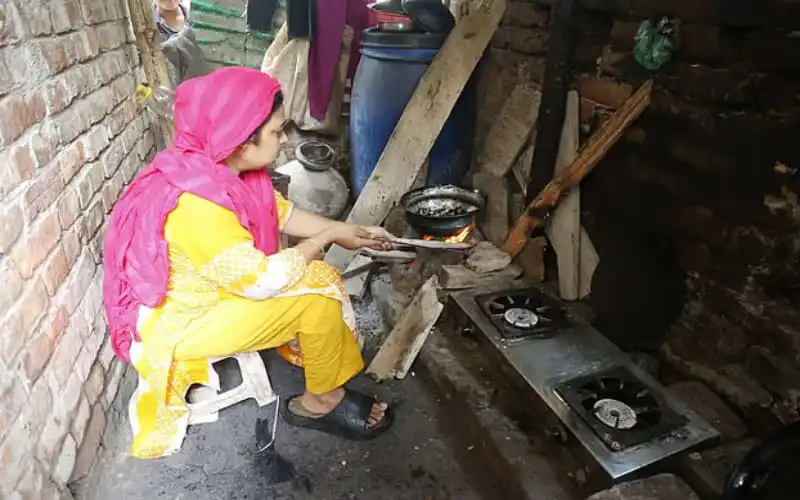 একজন নারী গ্যাস চুলার পাশে রান্না করছেন, পুরনো ঘরে।. Channel i News - চ্যানেল আই নিউজ