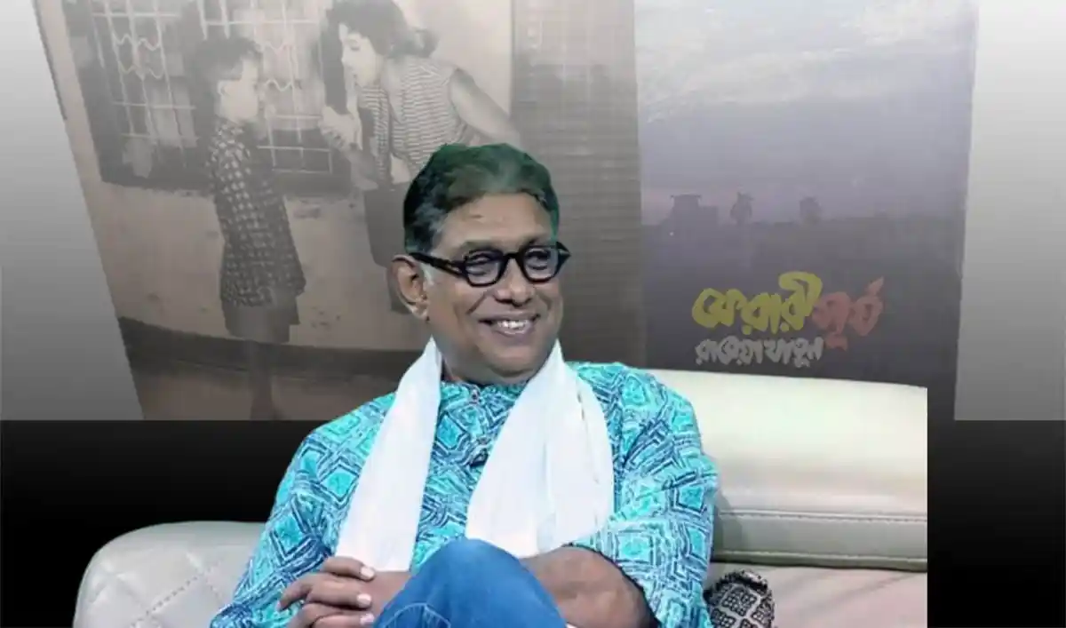 বঙ্গবন্ধু শেখ মুজিবুর রহমানের ছবি সহ একজন ব্যক্তি হাসিমুখে বসে আছেন. Channel i News - চ্যানেল আই নিউজ