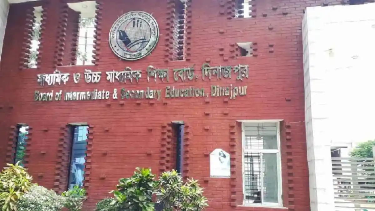 দিনাজপুর শিক্ষা বোর্ডের অফিস ভবনের ছবি, লাল ইটের দেয়াল ও গাছের সামনে. Channel i News - চ্যানেল আই নিউজ
