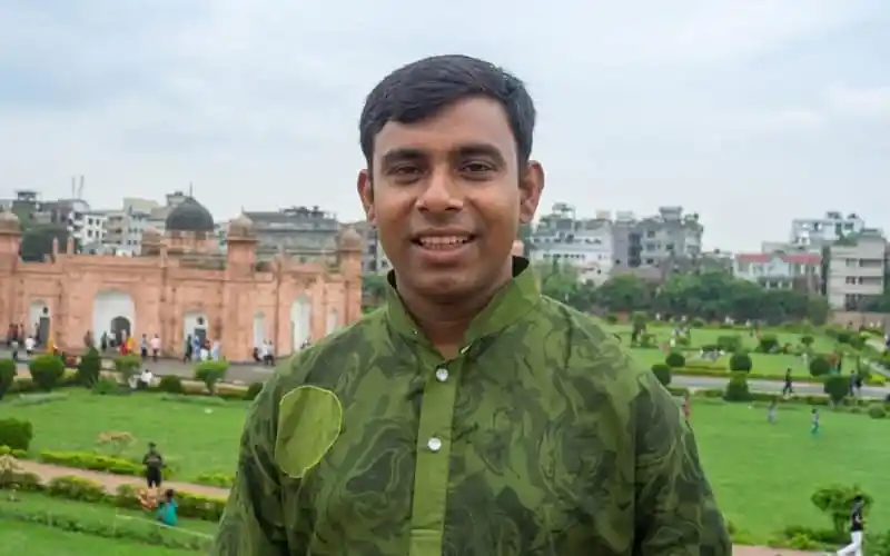 স্মার্ট যুবক ব্যক্তি সবুজ ক্যাজুয়াল পোশাকে, ঐতিহাসিক স্থাপনার পাশে দাঁড়ানো. Channel i News - চ্যানেল আই নিউজ