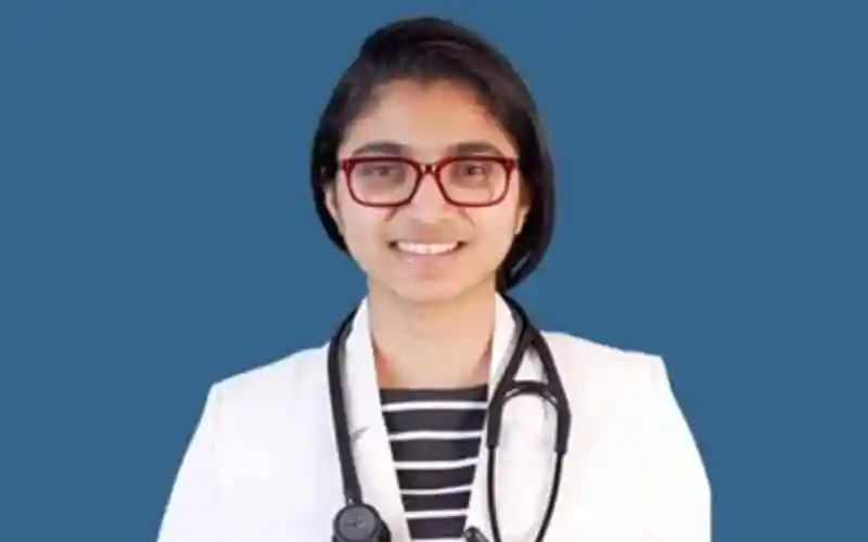 বাংলাদেশি নারী ডাক্তার হাসিমুখে, লাল চশমা পরা, সাদা কোটে. Channel i News - চ্যানেল আই নিউজ