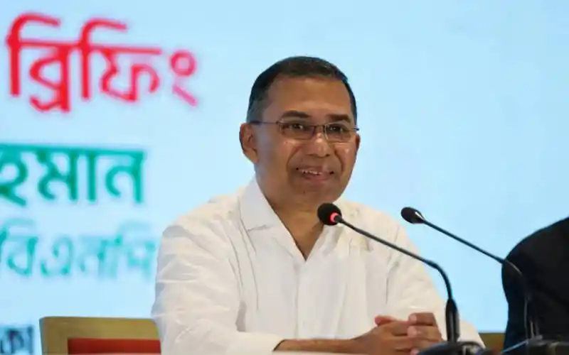 Bangladeshi politician speaking at a press conference with Channel i Online logo in background. Channel i News - চ্যানেল আই নিউজ