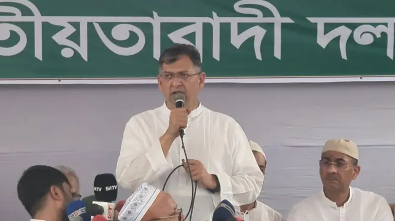 স্বরাষ্ট্রমন্ত্রী বক্তব্য দিচ্ছেন, পেছনে বাংলাদেশি পতাকা ও মঞ্চ. Channel i News - চ্যানেল আই নিউজ