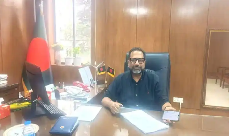 গৃহায়ন প্রতিমন্ত্রীর অফিসে বসে থাকা ব্যক্তি, বাংলাদেশ পতাকা পেছনে. Channel i News - চ্যানেল আই নিউজ