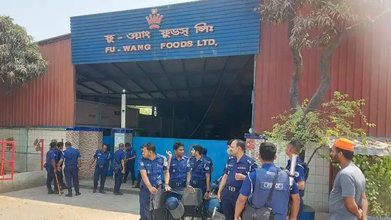 Fuwaang Foods factory with workers and security personnel outside during daytime. Channel i News - চ্যানেল আই নিউজ