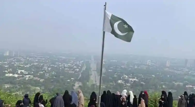 পাকিস্তানের পতাকা উঁচু করে দেখা যাচ্ছে, শহরের দৃশ্যের পেছনে. Channel i News - চ্যানেল আই নিউজ