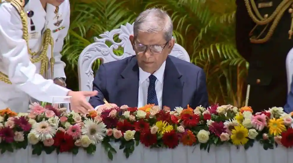 বৈঠকে একজন প্রবীণ ব্যক্তি ফুলের টেবিলের সামনে বসে আছেন. Channel i News - চ্যানেল আই নিউজ
